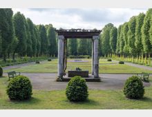 Ein gepflegter Park mit symmetrischen Rasenflächen, Wegen und Bäumen; im Vordergrund ein Pavillon mit vier Marmorsäulen und einer Pergola. Im Hintergrund liegt ein Blumenbeet in geometrischem Muster, flankiert von Hecken und Baumreihen.