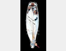 Luftaufnahme eines kleinen Segelbootes auf dunklem Wasser, mit einer ausgeklappten weißen Segelplane. Zwei Personen sitzen entspannt im Inneren des Bootes, das mit Holzdetails an Deck ausgestattet ist.