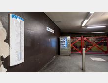 Unterirdischer U-Bahnhof mit einem Fahrplan der Linie U7 an der Wand, einem Getränkeautomaten und einer geschlossenen roten Gitterabsperrung im Hintergrund vor einer bunten Wandgestaltung.