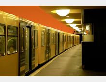 Gelber U-Bahn-Zug steht an einem beleuchteten Bahnsteig mit oranger Decke und runden Deckenlampen in einer unterirdischen Station.