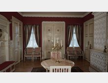 Ein historisch eingerichteter Raum mit roten Wänden, verzierten Holztüren, gestreiften Vorhängen und Polstermöbeln. Zentral steht ein runder Marmortisch mit einem goldenen Kerzenständer, während ein dekorativer Kachelofen die rechte Wand dominiert.