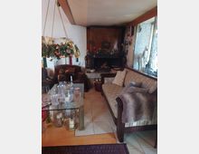 Gemütliches Wohnzimmer mit einer Sitzecke, bestehend aus einem gepolsterten Sofa und Sesseln, einem Kamin in einer dunklen Wandnische und einem Glastisch mit Kerzen. Die Dekoration umfasst weihnachtlichen Schmuck und Holzdetails, die den rustikalen Stil unterstreichen.