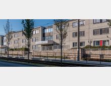 Mehrstöckiges Wohn- oder Bürogebäude mit hellgrauer Fassade und rechteckigen Fenstern, vor dem Gebäude befindet sich eine mit einem Geländer eingefasste erhöhte Terrasse und eine Straßenbahnhaltestelle. Einige Bäume und ein Straßenschild mit der Aufschrift „Leipziger Straße 53/54“ sind sichtbar.