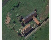 Luftaufnahme eines ländlichen Anwesens mit mehreren roten Ziegeldächern. Das Gelände umfasst ein Wohnhaus, Nebengebäude mit Solarpanelen, Gärten und angrenzende Wiesen.