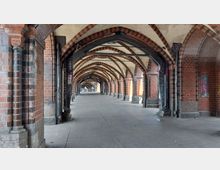 Ziegelsteingewölbe eines historischen Durchgangs mit Spitzbögen und Arkaden, abgestützt durch Metallträger. Die Wände sind mit roten und schwarzen Ziegeln gestaltet, manche Flächen zeigen Graffiti.