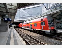 Bahnhof mit einem überdachten Bahnsteig und einem roten, doppelstöckigen Regionalzug der Deutschen Bahn an Gleis D5. Der Hintergrund zeigt moderne Glas- und Stahlarchitektur sowie eine Überführung.