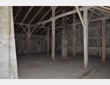 Ein leerer Dachboden mit sichtbaren Holzbalken und Dachkonstruktion. Die Wände sind aus Holz und Stein, und der Boden wirkt roh und unvollendet.