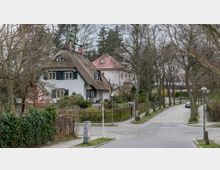Straßenszene in einer ruhigen Wohngegend mit einem weißen Fachwerkhaus mit Reetdach, umgeben von Bäumen und einem Garten. Die gepflasterte Straße ist von weiteren Einfamilienhäusern und Zäunen gesäumt, Straßenschilder weisen auf "Bittersstraße" und "Kreistraße" hin.