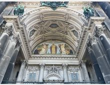Frontansicht eines reich verzierten Portals einer historischen Kathedrale mit korinthischen Säulen, detailliertem Dekor und einem farbigen Mosaik, das eine religiöse Szene zeigt, unterhalb eines kunstvoll gestalteten Bogens.