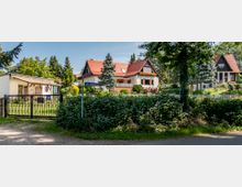 Wohngebiet mit Einfamilienhäusern, umgeben von Gärten und Bäumen. Im Vordergrund ein niedriges Gartentor, dahinter ein Weg und ein Straßenschild mit der Aufschrift „Am Petzinsee“.