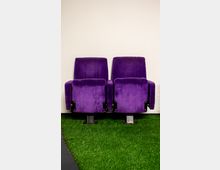 Zwei violette Kinosessel aus Samt sind nebeneinander an einer weißen Wand aufgestellt. Der Boden ist mit Kunstrasen bedeckt.