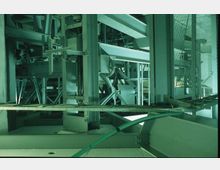 Ein Innenraum mit einer komplexen Stahlkonstruktion, bestehend aus Trägern, Stützen und maschinenähnlichen Elementen. Im Vordergrund ist ein grünes Kabel sichtbar, während im Hintergrund Metallgitter und Beleuchtung das technische Umfeld ergänzen.