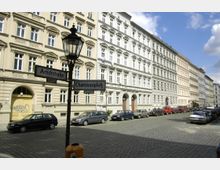 Straßenszene mit historischen Mietshäusern im Altbau-Stil, gepflasterter Straße und parkenden Autos. Ein Laternenpfahl mit Straßenschildern für „Arndtstraße“ und „Chamissoplatz“ steht im Vordergrund.
