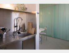Moderne Küchenzeile aus Edelstahl mit tiefem Spülbecken, hoher Spiralfeder-Armatur, Abtropfgitter und Küchenutensilien vor einer Metallrückwand. Rechts öffnet sich der Raum zu einem Essbereich mit rundem Tisch vor einer mintgrünen, gerippten Trennwand.