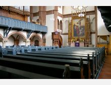 Innenraum einer Kirche mit hölzernen Kirchenbänken, einer reich verzierten Kanzel und einem Altar mit einem großen Gemälde der Kreuzigung. Sichtbare Elemente sind Backsteinbögen, eine umlaufende Galerie und eine Orgel im oberen Bereich.