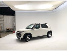 Ein weißer SUV steht in einem Fotostudio mit weißem Hintergrund und weicher Deckenbeleuchtung. Im Raum befinden sich Leitern, eine Putzmaschine und vereinzelte Requisiten am Rand.