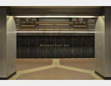 U-Bahn-Station mit der Aufschrift "Haselhorst" an einer dunklen Wand. Der Boden besteht aus beige- und braunfarbenen Fliesen, während die Decke mit Metallstreben und Beleuchtungselementen gestaltet ist.