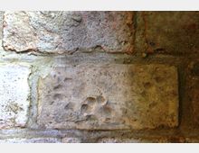 Nahaufnahme einer alten Ziegelsteinmauer mit sichtbaren Spuren eines Tiertatzenabdrucks auf einem Ziegel. Die Ziegel sind unregelmäßig verfärbt und mit Mörtel verbunden, was auf ein historisches Bauwerk hindeutet.