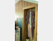 Ein traditioneller Kimono in lila und beige hängt an einem Holzkleiderbügel in einer Nische mit holzvertäfelten Wänden. Links daneben steht eine Spielküche und eine Kreidetafel.
