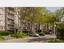 Mehrstöckiges Wohnhaus in einer urbanen Umgebung, mit Balkonen und Grünflächen im Vordergrund. Geparkte Autos stehen entlang einer Straße, die von Bäumen gesäumt ist; ein Straßenschild mit der Aufschrift „Kyritzer Straße“ ist sichtbar.