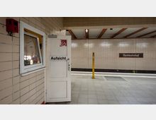 Innenansicht eines U-Bahnhofs mit beigefarbenen Fliesenwänden. Im Vordergrund ist eine weiße Tür mit der Aufschrift „Aufsicht“, daneben ein Fenster; im Hintergrund ist ein Schild mit der Aufschrift „Nordbahnhof“ und ein gelber Notruf- oder Informationspfosten sichtbar.