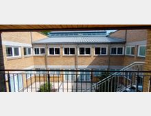 Innenhof eines modernen Backsteingebäudes mit zwei Etagen. Der Hof ist von gelben Backsteinwänden mit großen Fenstern umgeben, und eine Außentreppe führt entlang der rechten Seite.