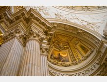 Innenansicht einer reich verzierten Kuppel in einer Kirche mit geschnitzten Säulenkapitellen im korinthischen Stil, goldenen Ornamenten und einem Mosaik des Evangelisten Matthäus, umgeben von Reliefdarstellungen und filigranen Details.