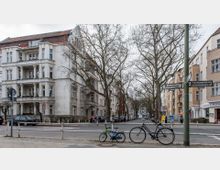 Straßenszene mit mehrstöckigen Wohnhäusern im Altbaustil, teils mit Balkonen, und kahlen Bäumen am Straßenrand. Im Vordergrund stehen zwei Fahrräder, Straßenschilder zeigen auf die Rubensstraße, und im Hintergrund sind Autos und geparkte Fahrzeuge zu sehen.