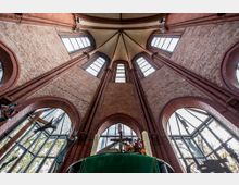 Innenansicht einer neugotischen Backsteinkirche mit einem hohen, gewölbten Dach und mehreren spitzbogigen Fenstern. Im Vordergrund stehen Kerzen und liturgische Elemente auf einem Altar mit grünem Tuch.