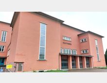 Außenansicht eines rosa gestrichenen Gebäudes mit der Aufschrift "Stadttheater". Das Gebäude hat eine klare, funktionale Architektur mit hohen vertikalen Fenstern und einem Eingangsbereich mit mehreren geschlossenen Metallgittern.