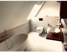 Modernes Badezimmer mit Dachschräge, ausgestattet mit freistehender Badewanne, wandhängender Toilette und Bidet, sowie einem Waschtisch mit Aufsatzwaschbecken auf einer Holzplatte. Natürliche Beleuchtung fällt durch ein großes Dachfenster ein.