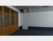 Ein leerer Innenraum mit weiß gestrichener Ziegelwand und dunkelblauer Sockelleiste. Links befinden sich Holztüren mit Glaseinsätzen, die den Raum abtrennen, und die Decke besteht aus rechtwinkligen weißen Deckenplatten, von denen einige fehlen.