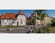 Fachwerkhaus mit Satteldach, beschriftet als "Museum", steht an einer gepflasterten Platzanlage mit Sitzbänken und jungen Bäumen; rechts daneben ein gelbes, mehrstöckiges Gebäude mit historischen Stilelementen. Im Hintergrund befindet sich eine Kirchturmspitze.