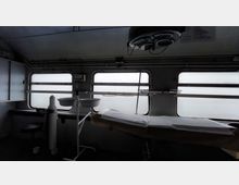 Innenraum eines mobilen Behandlungsraums mit metallenen medizinischen Geräten, einer Untersuchungsliege mit weißem Papierbezug und einem Hängelicht an der Decke. Die Fenster sind milchglasartig und lassen diffuses Licht in den Raum.