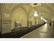 U-Bahnhof Heidelberger Platz mit hohen, cremefarbenen Gewölbedecken, verzierten Bögen und hängenden Laternen. Der Bahnsteig ist mit dunklen Fliesen verkleidet, an den Wänden befinden sich historische Fotografien.