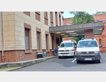 Zwei Rettungswagen stehen vor einem Gebäude mit beiger und roter Klinkerfassade unter einem überdachten Eingangsbereich. Im Hintergrund sind weitere Teile des Gebäudes mit roten Ziegeln und Bäume zu sehen.