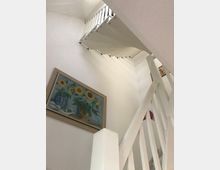 Eine weiße, moderne Wendeltreppe mit Geländer in einem hellen Innenraum. An der Wand hängt ein Gemälde mit Sonnenblumen in Vasen.