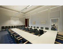 Konferenzraum mit rechteckig angeordneten Tischen und gepolsterten Stühlen mit Armlehnen, an den Wänden hängen Bilder und ein leerer Projektionsbereich ist sichtbar. Der Raum hat helle Wände, eine hohe Decke und einen dunklen Teppichboden.