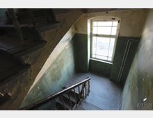 Engl: Eine verlassene Treppe in einem alten Gebäude mit abblätternder Farbe an den Wänden und einem großen Fenster.