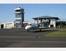 Ein kleiner Flughafen mit einer Flugzeughalle, einem Kontrollturm mit der Aufschrift "EDAZ" und einem modernen Terminalgebäude. Im Vordergrund steht ein geparktes Privatflugzeug auf dem Rollfeld, umgeben von einer asphaltierten Fläche und Grünflächen.