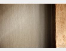 Nahaufnahme einer strukturierten Wand mit vertikalem Linienmuster in Beige- und Grautönen, rechts ein Abschnitt einer grob strukturierten Wand in warmen Erdtönen.