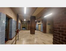 Ein Korridor mit Backsteinpfeilern, gefliestem Boden und blau gekachelten Wänden. Am Ende des Korridors führt eine Tür mit der Aufschrift „Kleine Schwimmhalle“ in einen weiteren Raum.