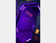 Futuristisch gestalteter Eingang in violettem Licht, umrandet von leuchtenden Neonröhren. Im Inneren sind Wände mit Schildern und Postern versehen, darunter ein Schild mit der Aufschrift „Gateway St. Authorized Personnel Only", sowie ein Bedienfeld mit leuchtender „Scan"-Anzeige.