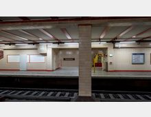 U-Bahn-Station mit dem Namen „Nordbahnhof“, gekennzeichnet durch beige geflieste Wände mit roten Akzenten. Im Hintergrund ist ein einfahrender gelb-roter Zug sichtbar, sowie Informationsschilder und ein beleuchtetes Notausgangsschild.