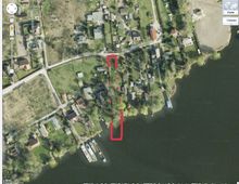 Satellitenbild eines Wohngebiets mit einzelnen Häusern, kleinen Grundstücken und Gärten, gelegen an einem Flussufer. Ein rotes Rechteck markiert ein bestimmtes Grundstück entlang des Wassers.