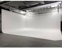 Großes Fotostudio mit nahtlosem weißen Hintergrund (Hohlkehle) und einem Betonboden. Die Decke ist mit Metallträgern und Beleuchtungsbefestigungen ausgestattet.