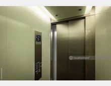 Moderner Aufzug mit glänzenden Metalltüren und Wänden aus hellem Material. Auf der linken Seite befindet sich eine Bedientafel mit beleuchteten Knöpfen und einer Digitalanzeige, die die Etage „4“ anzeigt.