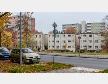 Wohnsiedlung an einer Straßenkreuzung mit mehrstöckigen Wohngebäuden im Hintergrund und niedrigeren, rechteckigen Wohnhäusern im Vordergrund. Vor den Häusern stehen Autos geparkt, es gibt Bäume mit herbstlichem Laub und ein Straßenschild mit der Aufschrift "Dorstener Straße".