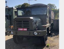 Militärisches Transportfahrzeug in olivgrüner Lackierung, geparkt auf einem gepflasterten Gelände. Das Fahrzeug hat eine robuste Front mit einem Schutzgitter, eine Plane über der Ladefläche und ein französisches Kennzeichen.