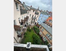 Blick auf einen Innenhof umgeben von mehrstöckigen Wohngebäuden mit Balkonen. Der Hof ist begrünt, mit Bäumen, Sträuchern und Rasenflächen, umgeben von gepflasterten Wegen.